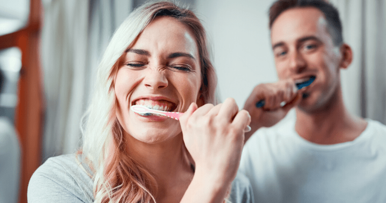 A blonde woman and brunette man brushing their teeth following the dental tips for quarantine by Dr. Rule