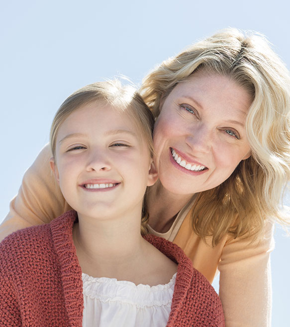 A middle-aged mother and young daughter happily smiling