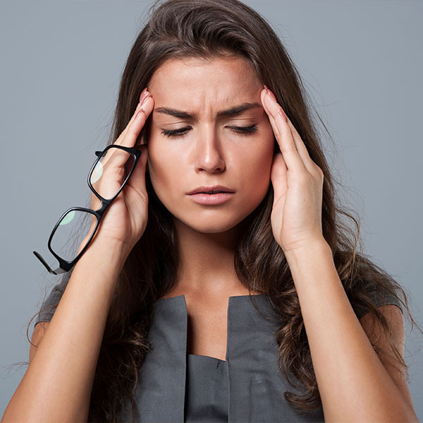 Woman in a grey skirt with glasses in her right hand on grey studio background having a headache